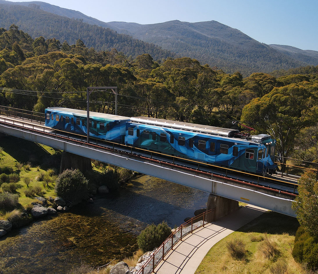Ski Tube on the Bridge Ski Tube train with blue abstract artwork crossing a bridge in the Snowy Mountains.