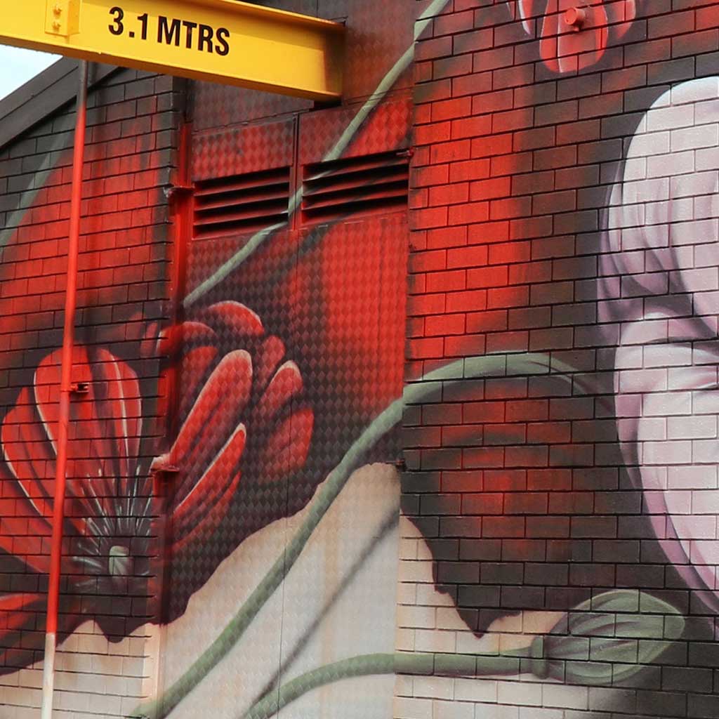 Detail of Anzac memorial mural at Currumbin RSL, featuring a realistic portrait and red poppies painted on metal and brick surfaces