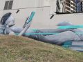 Large-scale Brisbane mural at South Bank depicting a reclining figure reading, painted in a realistic grayscale style with turquoise graphic elements, by Mike Shankster.