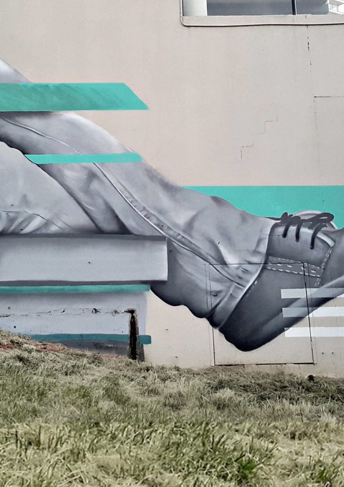 Detail of a Southbank mural showing a grayscale figure’s legs and shoes with turquoise geometric lines on a concrete wall.