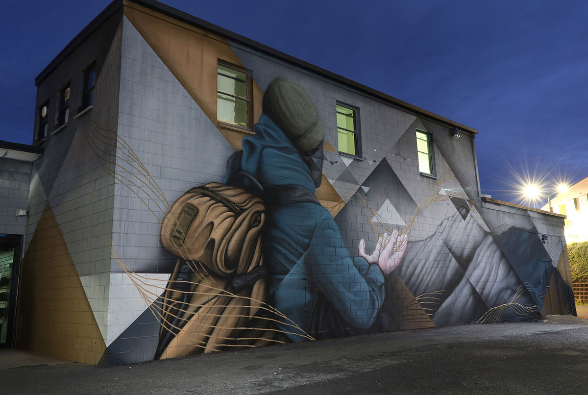 Jindabyne Sentinel mural, exterior wall Large scale mural in Jindabyne depicting a hooded figure with backpack, painted across an exterior building wall at night