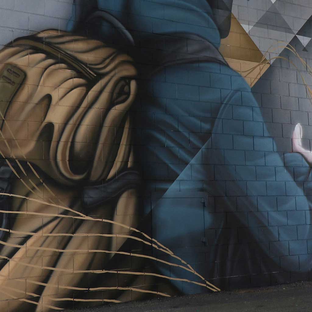 Detail of Jindabyne Sentinel mural showing a hooded figure with backpack painted on brick wall