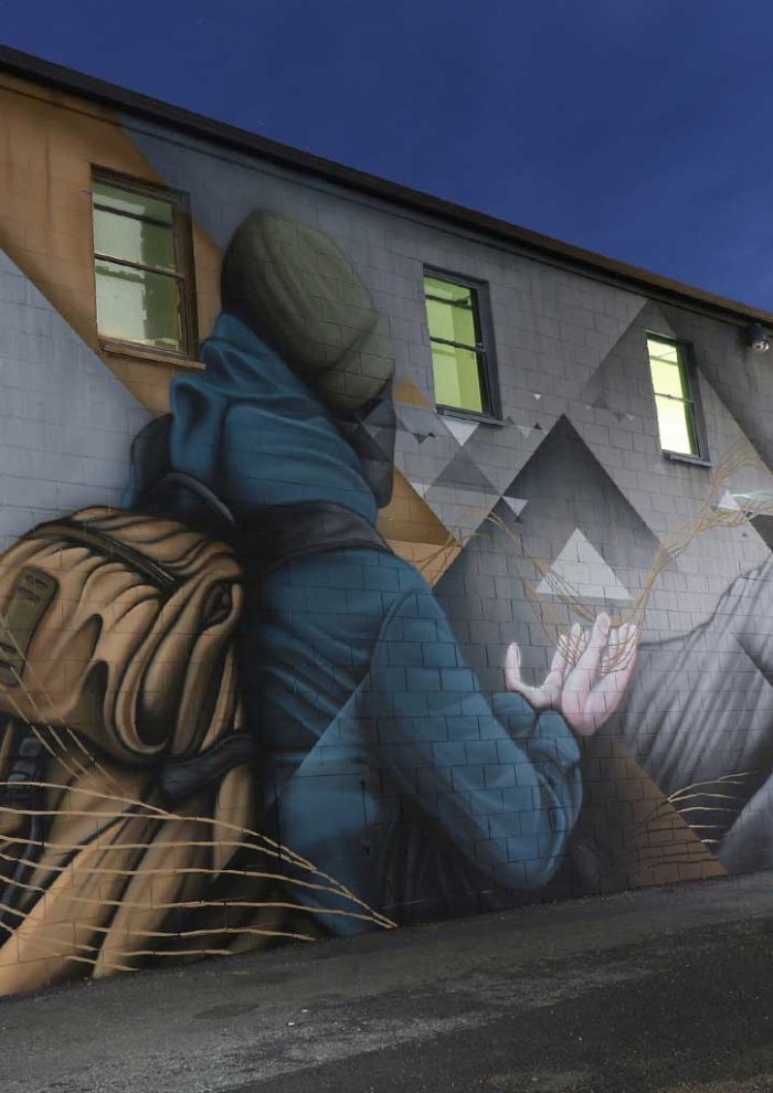 Detail of Jindabyne Sentinel mural showing a hooded figure with backpack painted on brick wall