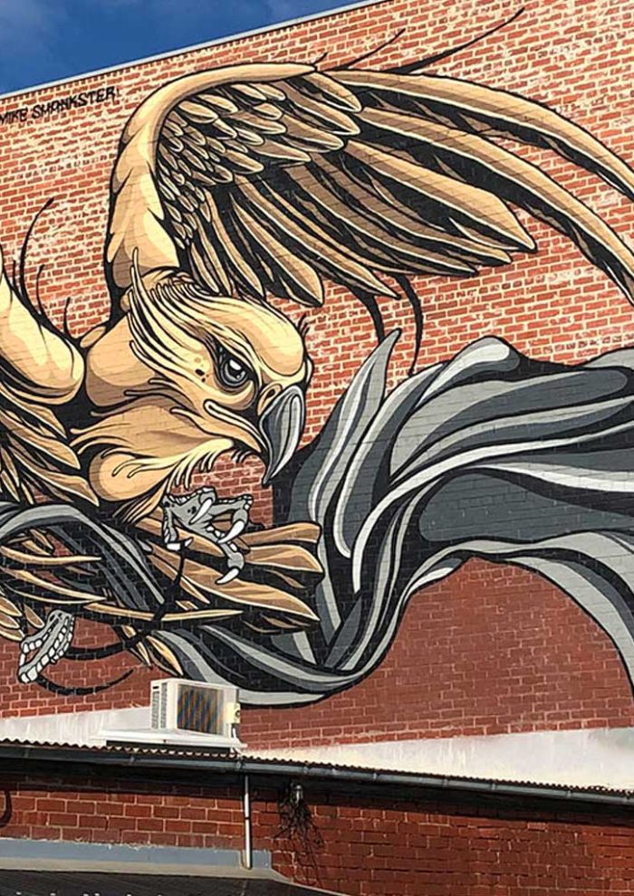 Large eagle mural across a red brick building, with sweeping black and grey ribbon forms, by Mike Shankster
