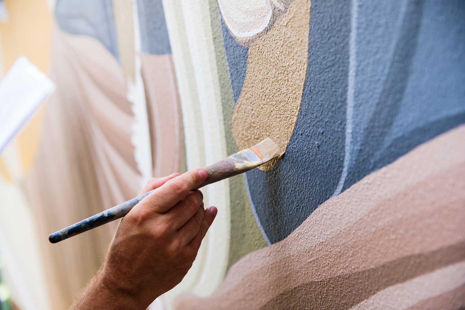 Close-up of a paintbrush applying colour on a textured wall during the Warry Street mural, Brisbane