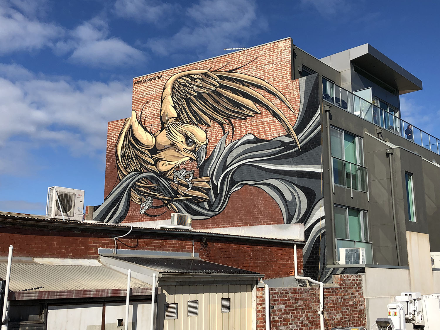 Large eagle mural across a red brick building, with sweeping black and grey ribbon forms, by Mike Shankster