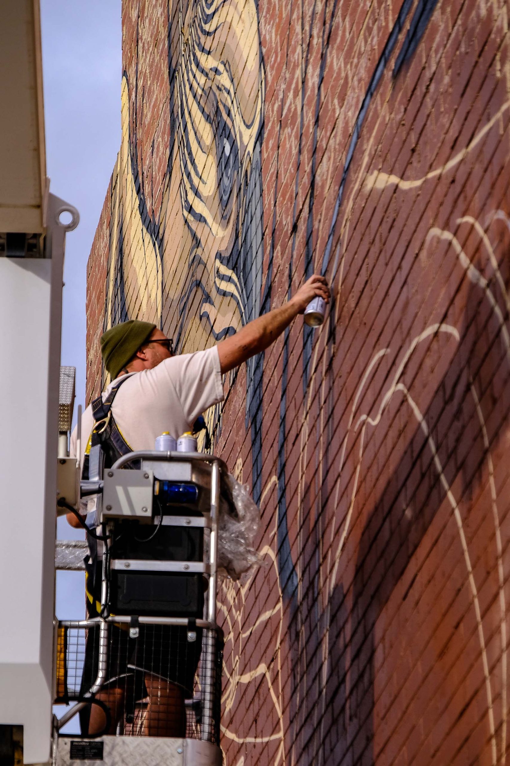 Artist on a boom lift spray painting linework on a brick wall, building a large eagle mural