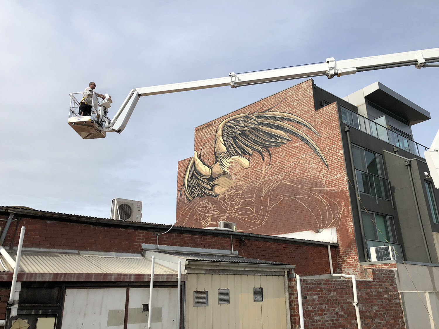 Boom lift extended to a brick wall as the eagle mural is painted, with sketch layout lines below