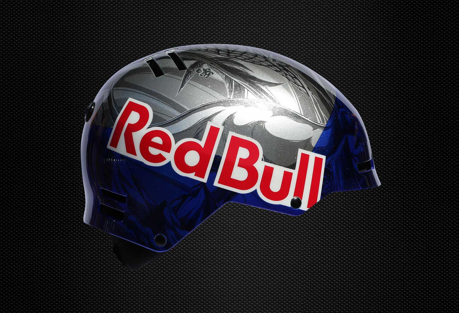 Red Bull helmet graphic, side logo view, Russ Henshaw Side view of a Red Bull helmet with metallic silver and deep blue custom graphics and large Red Bull wordmark on a black textured background.