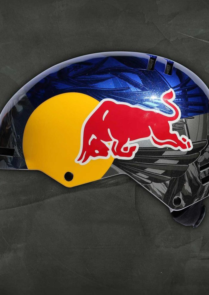 Red Bull helmet with custom blue and black graphic design, photographed on a dark textured background.