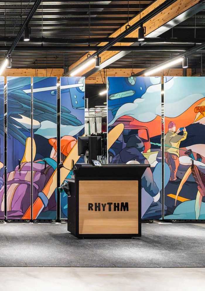 Illustrated in-store banner panels behind Rhythm checkout counter, showing snow travel scenes, mountains, and riders