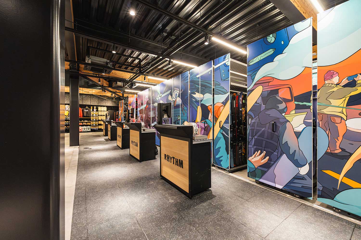 Angled view of Rhythm Japan checkout row with tall illustrated banner panels on sliding racks, featuring riders and mountain scenes