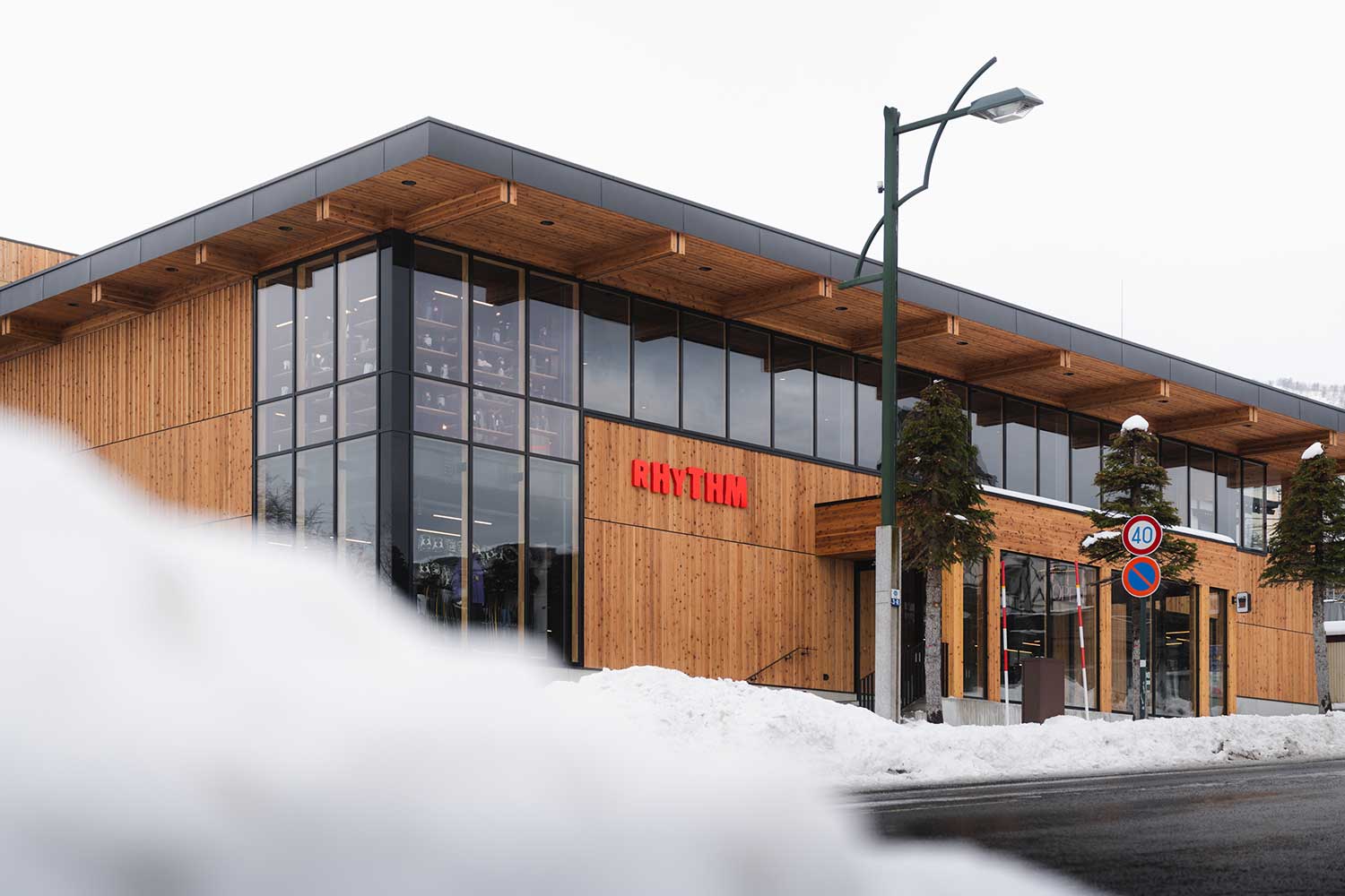 Exterior of Rhythm Japan store with timber cladding and large RHYTHM sign, snow piled along the street