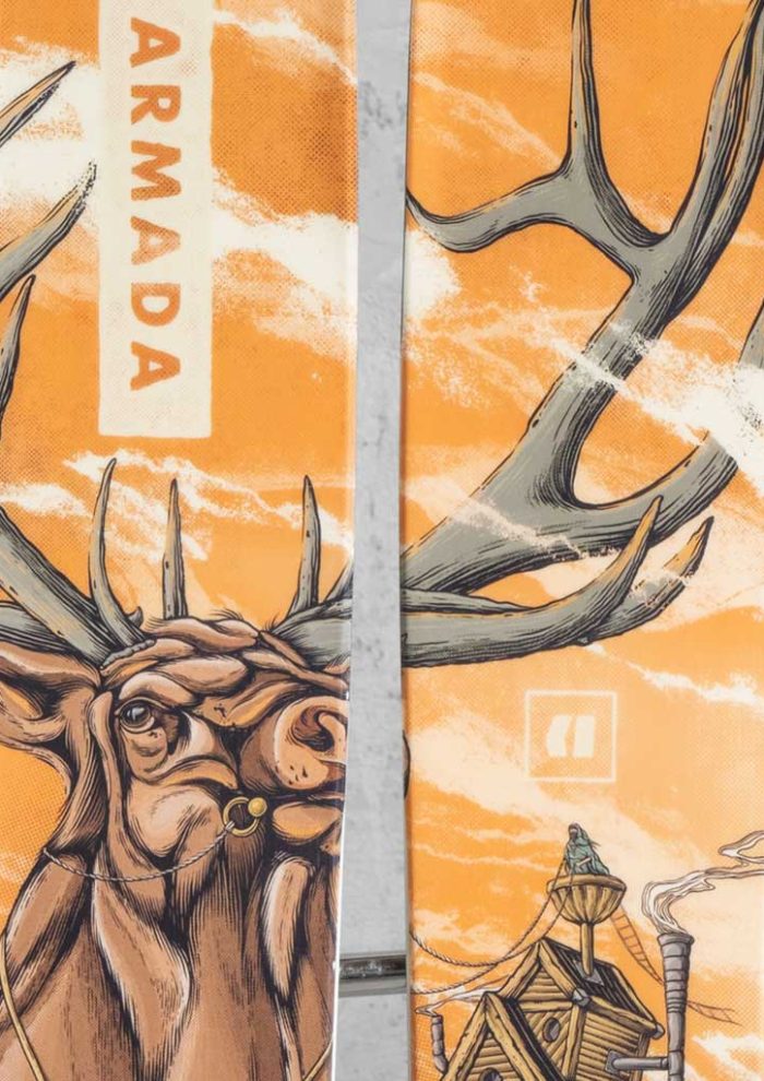 Close-up of Armada skis featuring custom elk illustration artwork in orange tones, with large antlers spanning across both skis.