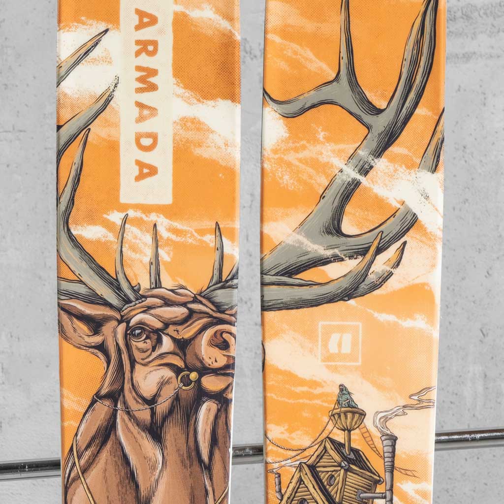 Close-up of Armada skis featuring custom elk illustration artwork in orange tones, with large antlers spanning across both skis.