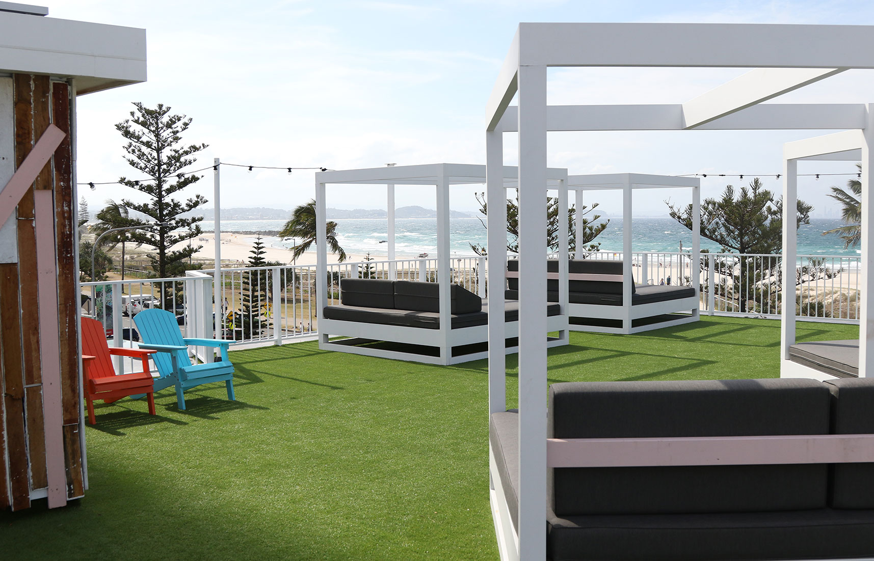Rooftop bar area at The Pink Hotel in Coolangatta, with white cabanas, lounge seating, artificial turf, and ocean views.
