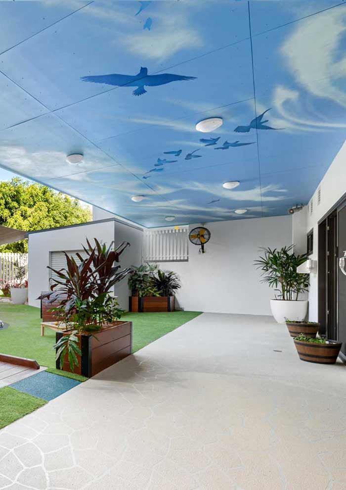 Blue sky ceiling mural with birds and clouds painted over a childcare centre outdoor play space on the Gold Coast.