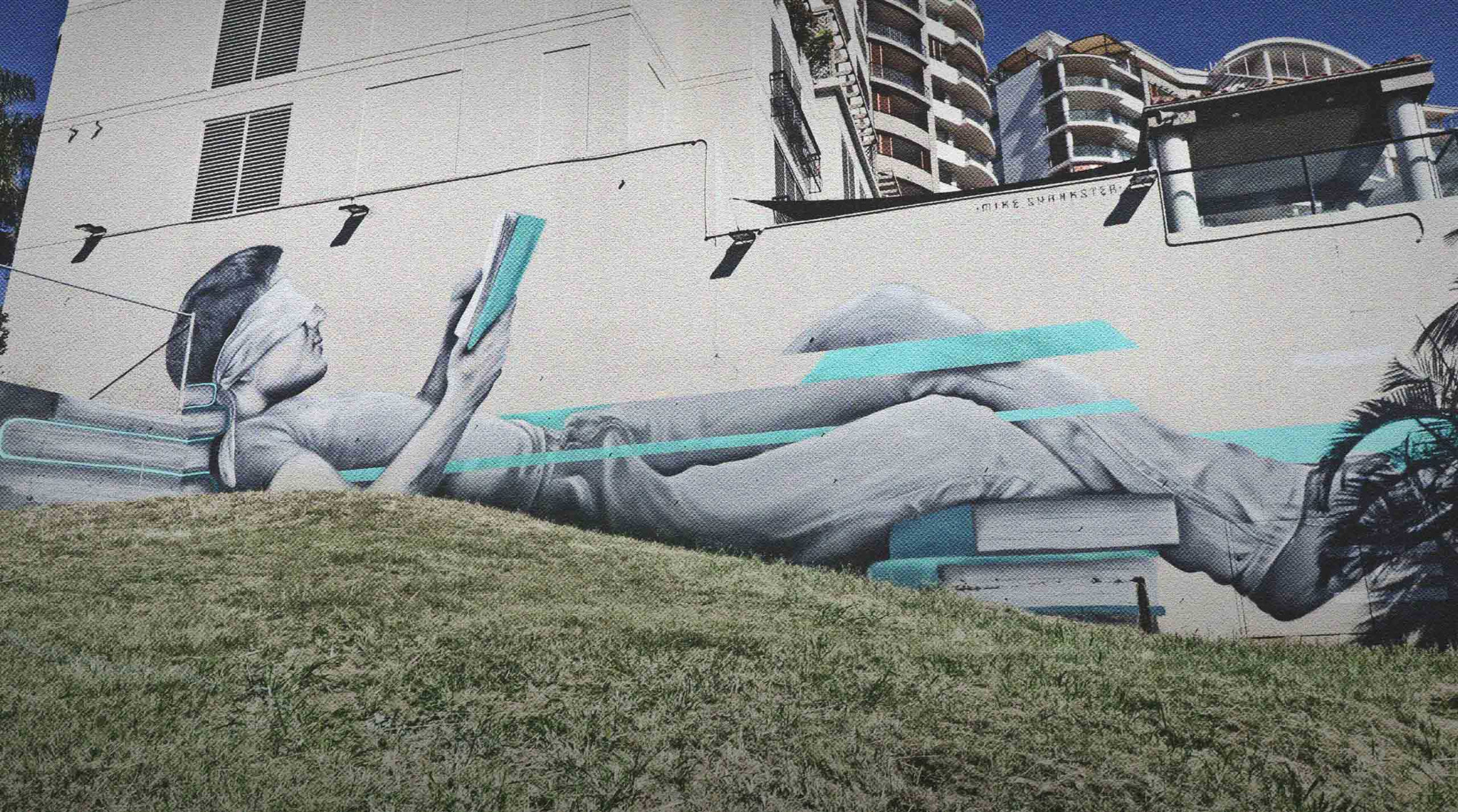 Large-scale South Bank mural by Mike Shankster featuring a reclining figure reading, painted across an exterior building wall in Brisbane.